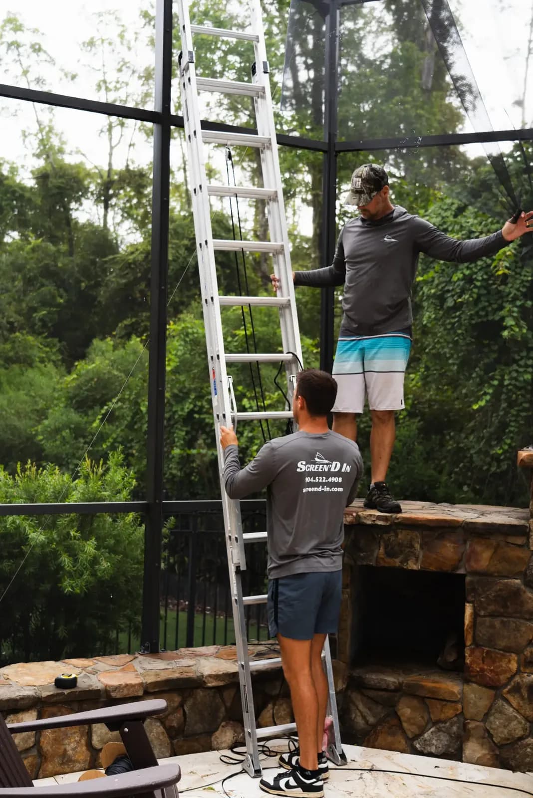 Two Screen'D In crew members setting an extension ladder in branded shirts