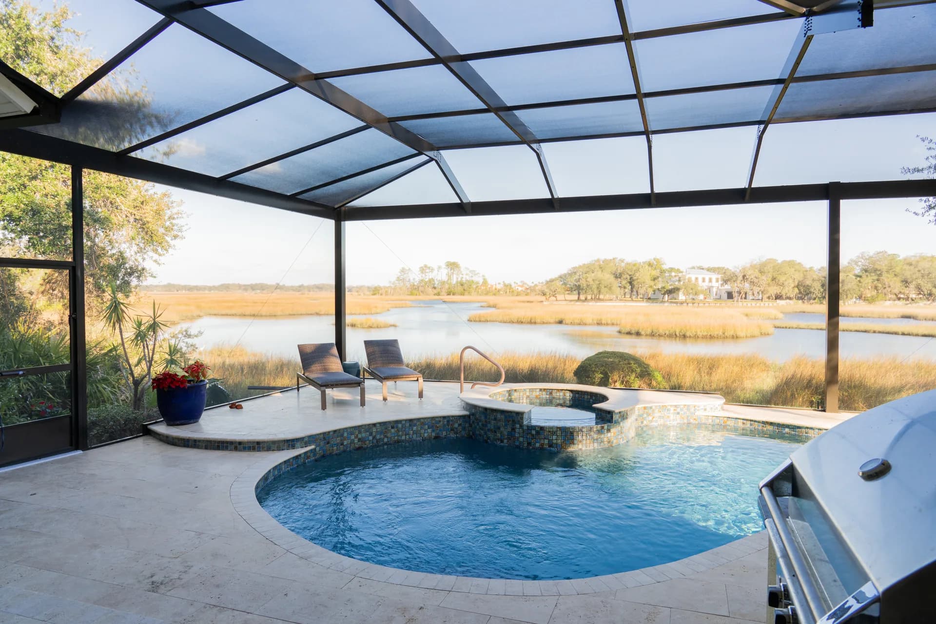 Screened pool, spa, and travertine deck overlooking a Florida marsh