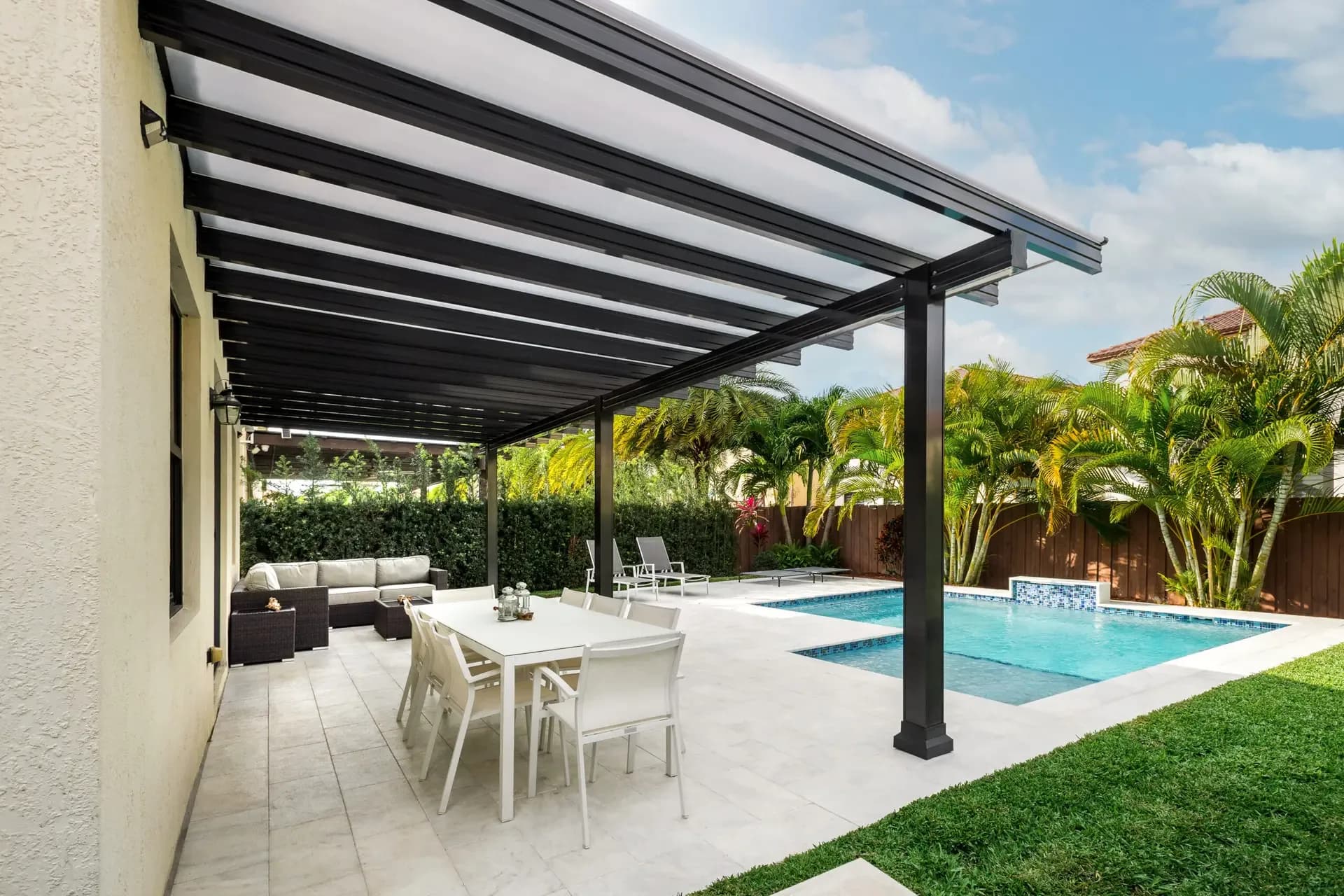 Black aluminum pergola over a dining patio beside a backyard pool